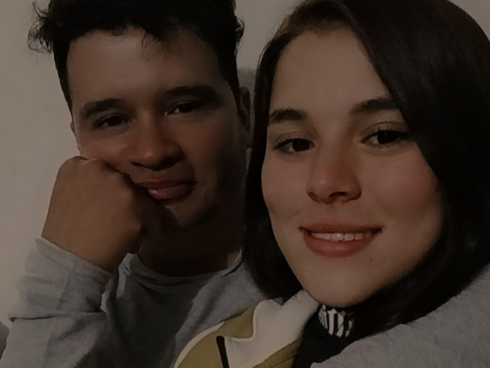 AmyyAlan, con i capelli neri e la pelle chiara, sorride ed è accanto a un uomo con i capelli scuri e la pelle chiara, entrambi con il mento appoggiato sulle mani..