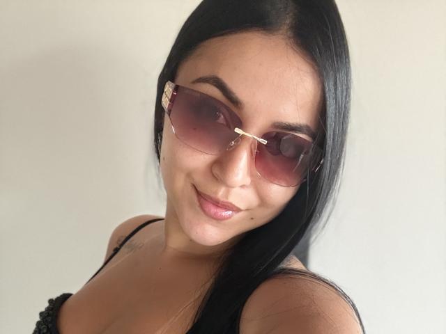 HikariChloe tiene el cabello negro oscuro, gafas de sol con un ligero tono rosa y una sonrisa encantadora con labios rosados y brillantes. Lleva un top negro con tirantes que deja ver sus pequeños senos..