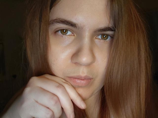 Mathilda Lovejoy tem olhos castanhos, pele clara e cabelos longos castanhos. Ela está apoiando o queixo na mão, com uma expressão neutra e ligeiramente emburrada. Seus mamilos não estão visíveis..
