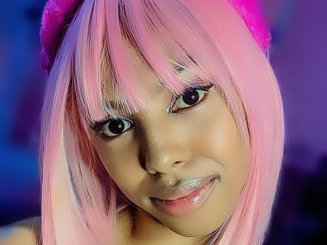 MissAniaSexy a les cheveux roses, des yeux foncés avec de longs cils, et une bouche brillante, légèrement entrouverte. Elle porte un chapeau rose en fourrure, et sa peau est d'une teinte marron chaud..