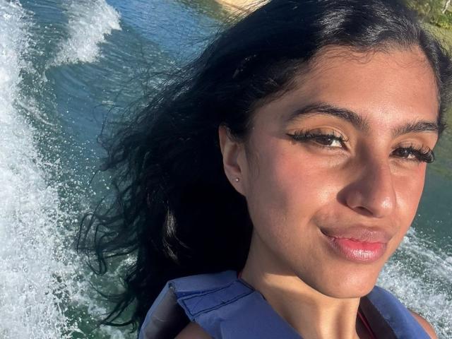 LilithDesire ha la pelle marrone chiaro, lunghi capelli neri ed è sorridente, con labbra leggermente rosate e lucide. Indossa un giubbotto di salvataggio blu, e sullo sfondo si vedono schizzi d'acqua..