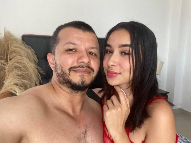 LaylaAndJoshua com barba preta curta e LaylaAndJoshua com vestido vermelho e cabelo preto, ambos sorrindo, peito com peito, a mão de LaylaAndJoshua no pescoço de LaylaAndJoshua, LaylaAndJoshua sem camisa..