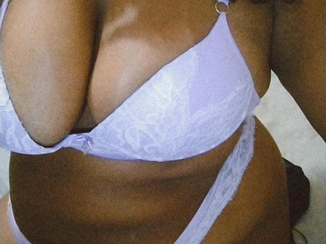 Los grandes, marrones y desnudos senos de Memell, en un sujetador y tanga de encaje color lila, mostrando su vientre curvilíneo y de piel oscura, y un ombligo pequeño y visible..