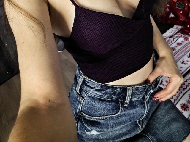 De zwarte bh van YourRedFlag, met zichtbare decolleté, die haar borsten laat zien, gecombineerd met hoge, blauwe, gescheurde denim shorts, en haar hand op haar heup, met rode nagellak..