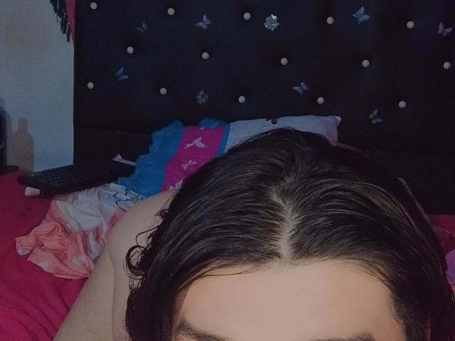 Het donkerbruine haar van Keissydoll is nat en verspreid over een roze bed, met een zwart hoofdeinde met franjes op de achtergrond en een blauw en roze kussen..