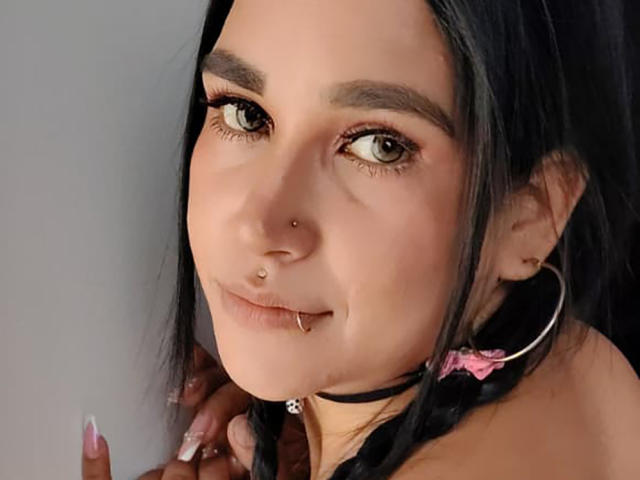 EdenIvyLm hat dunkles Haar, grüne Augen und mehrere Piercings im Gesicht: Nase, Lippe und Nasenscheidewand. Sie trägt eine schwarze Halskette mit einem rosa Band und große Ohrringe..