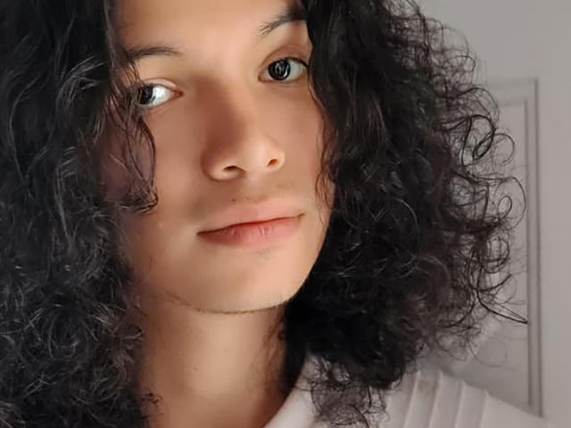 FrankieManHot a les cheveux noirs bouclés, une peau brun clair et une petite moustache. Les yeux de FrankieManHot sont verts et il regarde directement l'appareil photo avec un léger sourire..