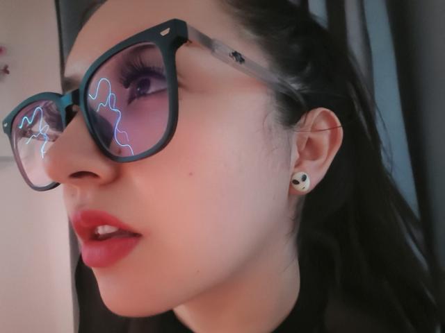 SusanMonroy with dark glasses reflecting neon lines, red lips slightly parted, black hair, white skin, small black earrings, looking to the side, close-up, wearing black top.