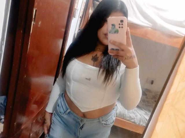 PartyLindaDestruction com cabelo preto longo, cropped branco de manga comprida, jeans azuis, segurando o celular cobrindo o rosto, tatuagem no peito, selfie no espelho, seios pequenos visíveis, quarto..