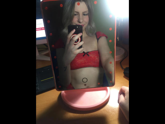 Étudiante - Très séduisante, avec une peau pâle et des cheveux blonds, portant un soutien-gorge en dentelle rouge, prenant un selfie dans un miroir à pois, tenant un téléphone, montrant un piercing au nombril..