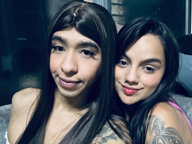 Haily hat langes, braunes Haar und ein süßes Lächeln, neben Alisa mit schwarzem Haar, pinkem Lippenstift und einem Tattoo auf ihrer Schulter, wobei beide ihre Brüste zur Schau stellen..