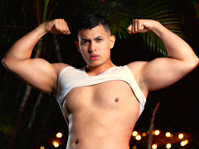 RomanCroft flexing muscular arms, wearing a white tank top pulled up to expose his chest and abs, with short dark hair and a serious expression, in a nighttime setting.