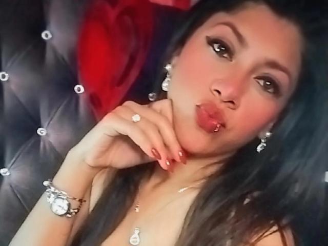NataliaCruz with dark hair, wearing diamond earrings and a bracelet, pouting her glossy pink lips, showing off her ring, with a cute, sexy look. Boobs partially visible.