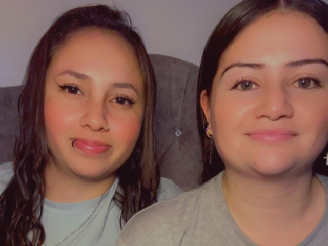 CandyAndHonney has medium brown skin, black hair, and is sticking her tongue out. Honney has lighter skin, brown hair, and is smiling. Both are wearing gray shirts.