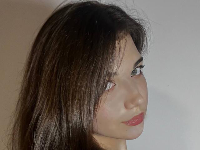 El rostro de ShellieBessmer, con su cabello castaño largo, ojos verdes y lápiz labial rojo, muestra una ligera sonrisa y un cutis claro y suave..