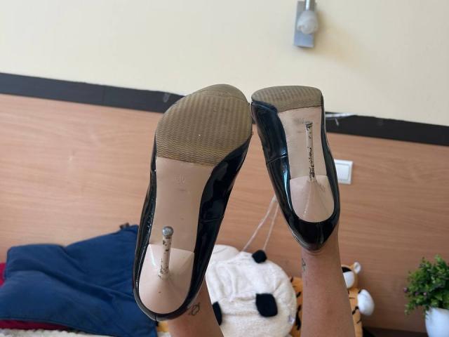 MoonLiza's black high heels with shiny soles, showing the textured bottom, are raised with her legs slightly apart, displaying a small metal spike on the heel.