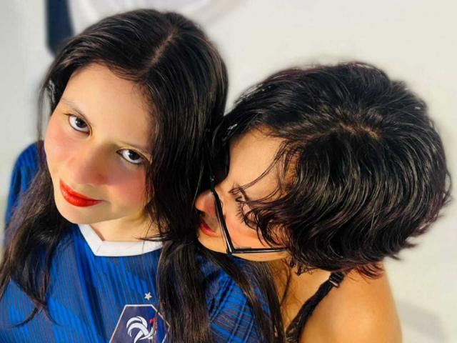 GabyDani con cabello largo y oscuro, lápiz labial rojo, camisa azul, y GabyDani con cabello corto y negro, gafas y correa negra, inclinándose, mostrando afecto..