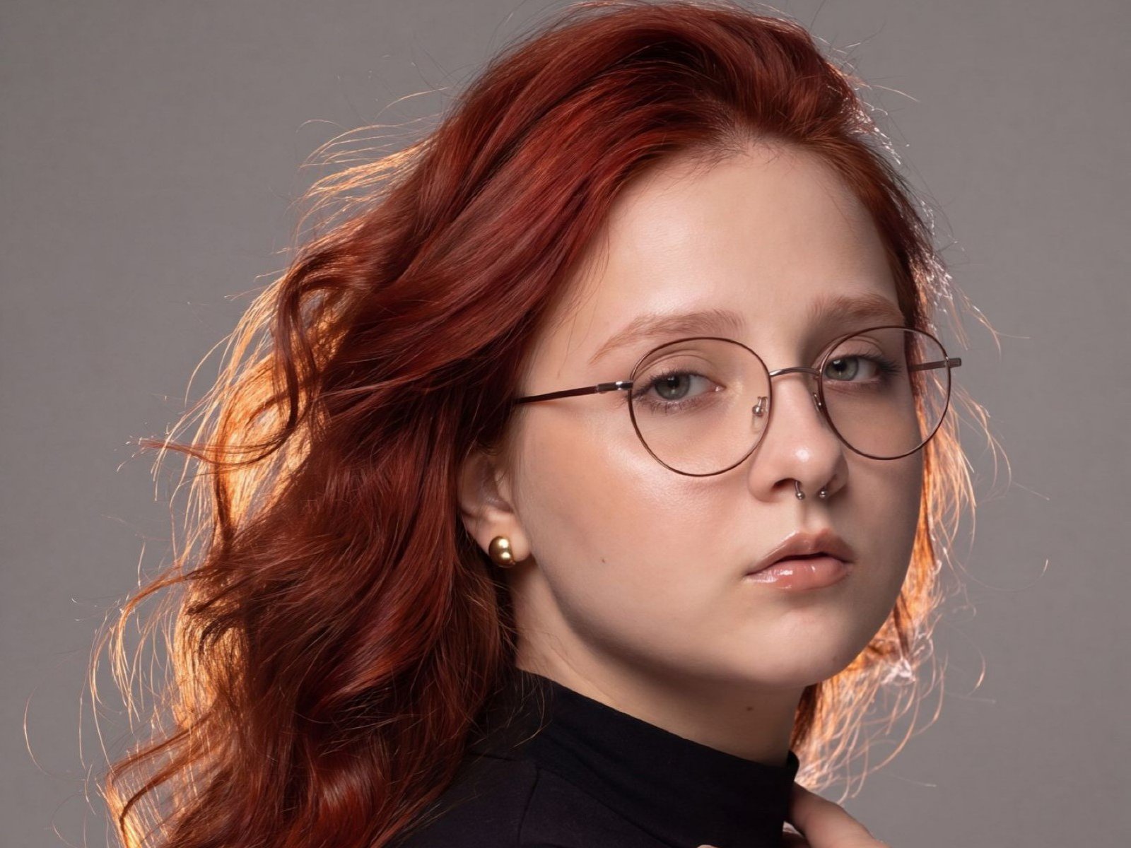 SaraMunewe heeft rood haar, ronde brillen, een neusring en een zwarte coltrui. Ze heeft een serieuze uitdrukking, een lichte huid en een kleine gouden oorbelle in haar linker oor..