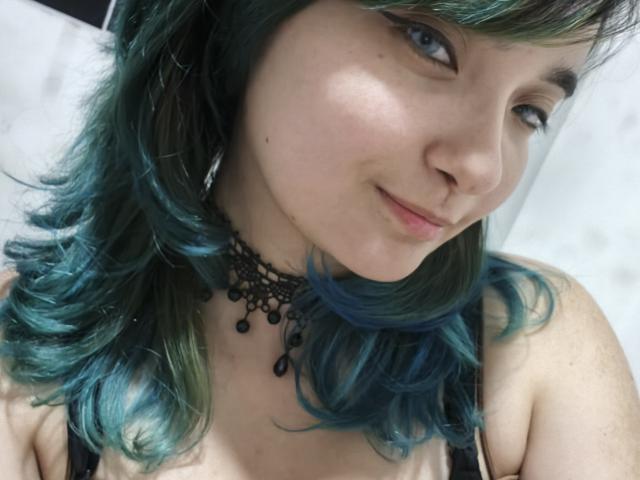NaommyCarter with teal blue hair, black lace choker, light skin, small nose, subtle smile, blue eyes, wearing black top, looking slightly to the right, slight blush on cheeks.