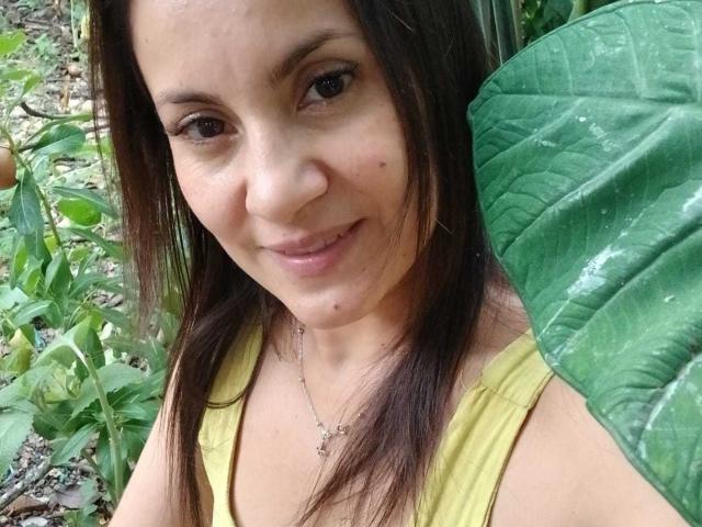 SolaraDubois, avec ses cheveux bruns, souriante, portant un débardeur jaune, montrant ses petites seins et une petite tache de rousseur sur sa joue droite, tenant une feuille verte..