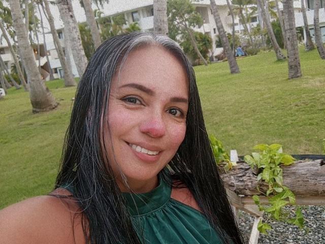 LailaCastillo has wet black hair, a cute smile, and a pink nose. She's wearing a green halter top, showing her tits, in a grassy outdoor setting.