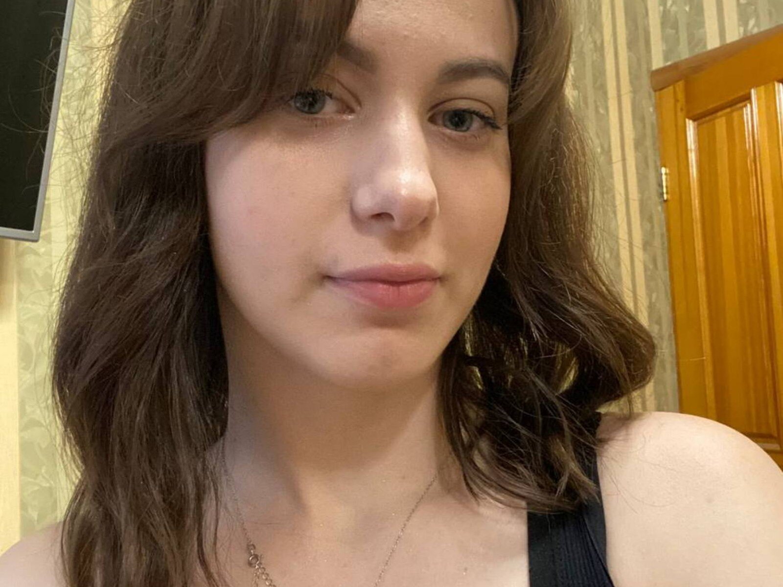 ShakitaDederick has brown wavy hair, light skin, subtle makeup, pink lips, and a silver necklace. She's wearing a black tank top, looking slightly up at the camera.
