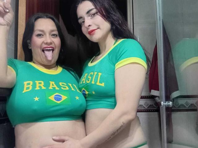SaraAndMarilyn69, zwei Frauen mit grünen brasilianischen Hemden, Saras große Brüste, Marilyn's kleine Brüste, Marilyn's Hand auf Saras Bauch, beide lächeln, Saras Zunge heraus, Marilyn's roter Lippenstift..