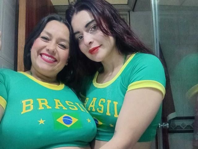 SaraAndMarilyn69, zwei Frauen mit grünen brasilianischen Hemden, gelben Akzenten und dem Schriftzug "Brasilien", stehen eng beieinander, lächeln, tragen roten Lippenstift, haben dunkles Haar, kleine Brüste, in einem Badezimmer..
