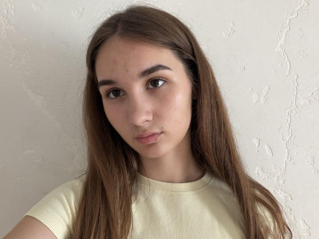 GracieJanuary tiene el pelo largo y castaño, ojos marrones y una expresión neutra. Lleva una camiseta amarilla de punto. Su rostro tiene algunas pequeñas imperfecciones..