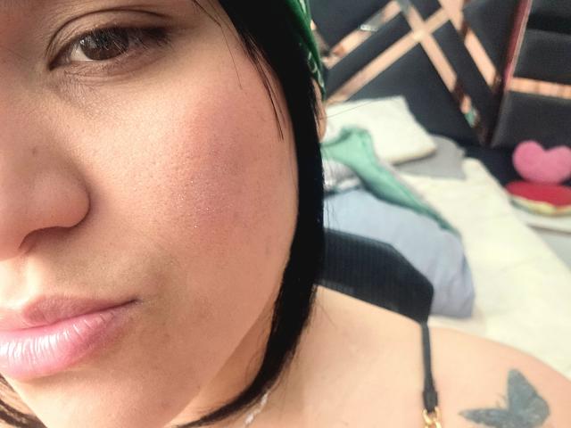 VivianaThompson's face, showing her puffy pink lips, light brown eyes, and green headband, with a black strap and butterfly tattoo on her shoulder.