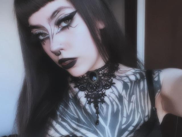 LitenKiitt a un maquillage gothique avec un eye-liner noir épais, un rouge à lèvres foncé, un anneau de nez et de longs cheveux noirs. Elle a des tatouages de motifs de zèbre et porte un collier en dentelle noire..