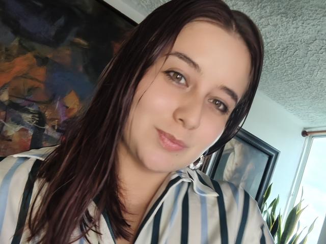 Angela Monticelli, con capelli marrone chiaro, occhi verdi e pelle chiara, indossa una camicia a righe, ha labbra leggermente rosate e lucide e un sorriso discreto, in una stanza ben illuminata..