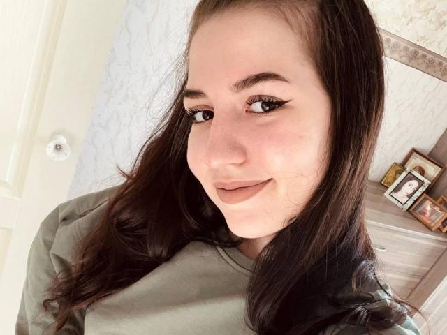 BethelVanhamme heeft lang bruin haar, een schattige glimlach en draagt een groene blouse. Haar eyeliner is scherp en ze heeft een kleine puist op haar rechterwang..
