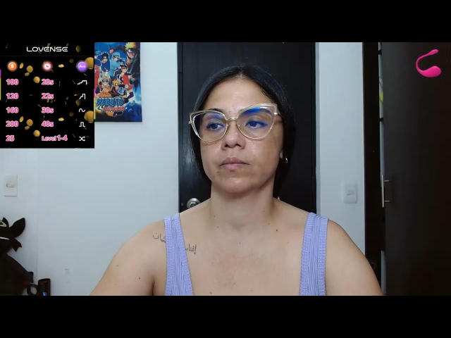 Selena Ferrri, mit blauen Augen, die eine klare Brille und ein violettes Tanktop trägt, hat ein Tattoo an ihrer rechten Schulter. Sie blickt direkt in die Kamera, mit einem neutralen Gesichtsausdruck..