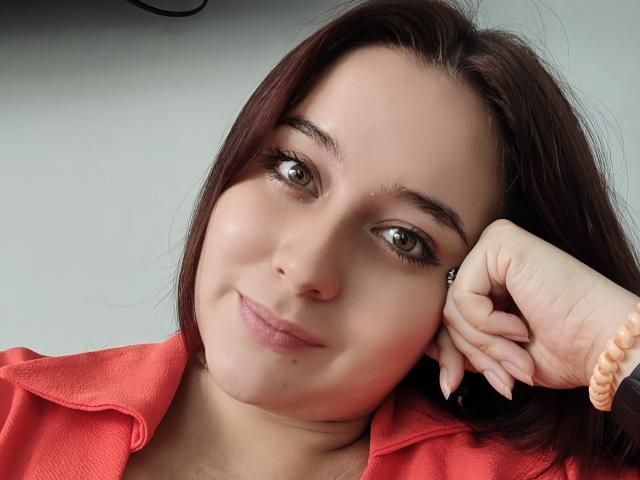 Angela Monticelli ha gli occhi marroni, i capelli castano scuro e un leggero sorriso. Indossa una camicia rossa, con la testa appoggiata sulla mano e un braccialetto rosa..