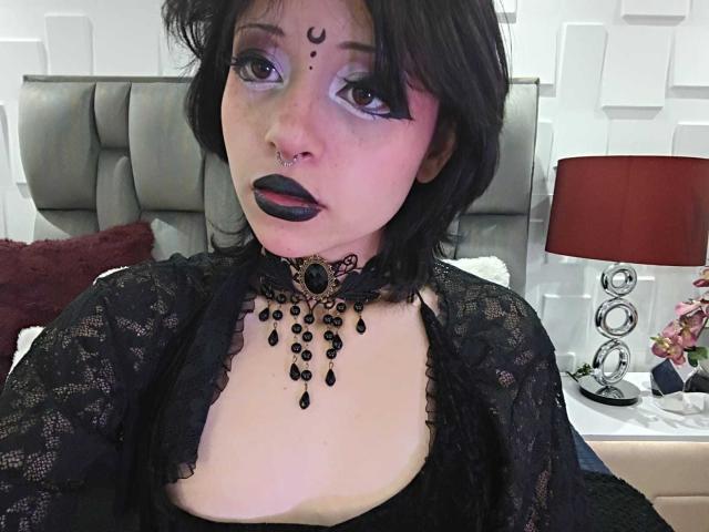 ViolettClay heeft zwarte lippenstift, een neusring en een tatoeage in de vorm van een traan op haar gezicht. Ze draagt een koordje met zwarte kralen en een zwarte kanten top, waardoor haar borsten zichtbaar zijn..