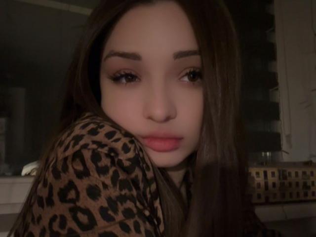 BreanaAdina with long brown hair, wearing a leopard print shirt, has full lips and dark eyebrows, looking slightly to the side with a subtle, pouty expression.