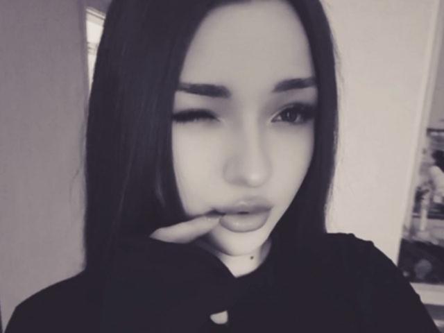 Black-and-white photo of BreanaAdina with long dark hair, winking, and touching her lips with her finger. She has full eyebrows, long eyelashes, and a small beauty mark.