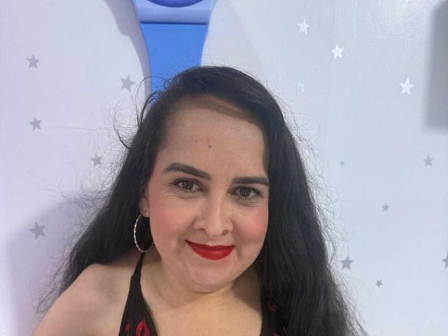 Diana Lane heeft lang zwart haar, rode lippenstift en draagt oorbellen. Ze draagt een zwart topje met rode patronen, waarbij haar borsten gedeeltelijk zichtbaar zijn..