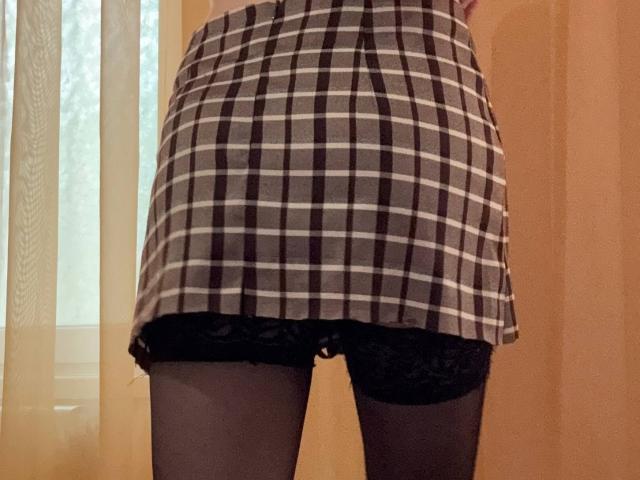 Il sedere di MiyaLia in una gonna a quadri bianco e nero, che mostra pizzo nero e calze nere trasparenti. La gonna è sollevata, rivelando la sua vulva coperta di pizzo..