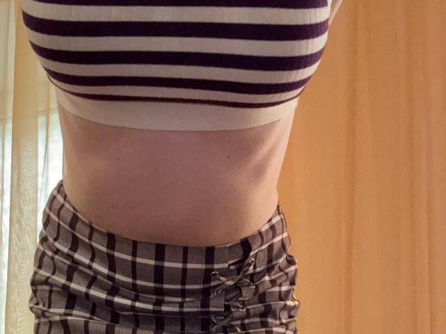 La sezione addominale sottile e chiara di MiyaLia rivela una canotta a righe, mettendo in mostra il suo ventre piatto. Indossa dei pantaloncini a quadri con bottoni, che evidenziano i suoi glutei piccoli e sodi..