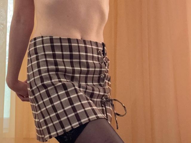 MiyaLias schlanke Taille und flache Bauchmuskeln sind zu sehen, wie sie einen braun-weißen karierten Rock mit Schnürung vorne, schwarze Strumpfhosen und kein Oberteil trägt, und sie steht in einem Holzraum..