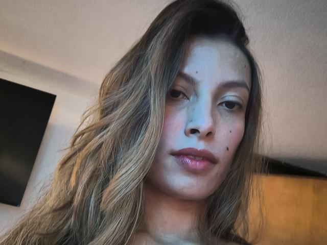 KiaraWiild tiene el cabello castaño ondulado, piel clara y algunas pecas en la cara. Está mirando a la cámara con los labios rosados, y lleva puesto un top negro..