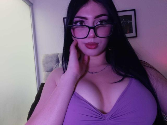 Isabella Rossi, com seios grandes, vestindo um vestido roxo, óculos pretos, cabelo preto longo, mão no rosto, batom vermelho, luz roxa, foto emoldurada ao fundo..