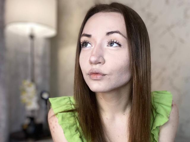 KatheyKuang with puffy lips, green ruffled top, brown straight hair, blue eyes, and long eyelashes, looking slightly to the side. Soft, pale skin with freckles.