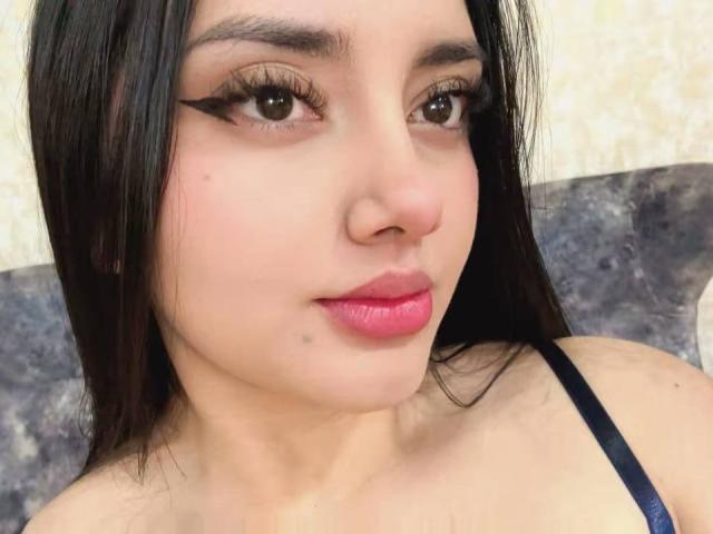 Amalia Dalton ha i capelli castano scuro, ciglia folte e rossetto rosa. La sua pelle chiara ha una piccola lentiggine sotto il labbro destro. Indossa un top nero con spalline..