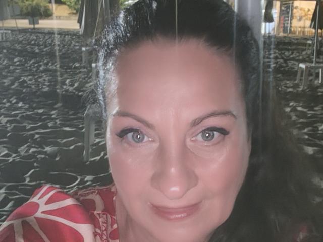Ein Selfie von Emerald mit hellblauen Augen, einem leichten Lächeln und strahlender Haut, die ein rotes, gemustertes Hemd trägt, wobei ihr Gesicht und ihr dunkelbraunes Haar zu sehen sind..