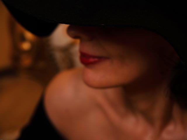 Il viso di KamiLove, parzialmente oscurato da un cappello nero, mostra labbra rosse e una spalla scoperta. La sua pelle è chiara e l'immagine è leggermente sfocata..