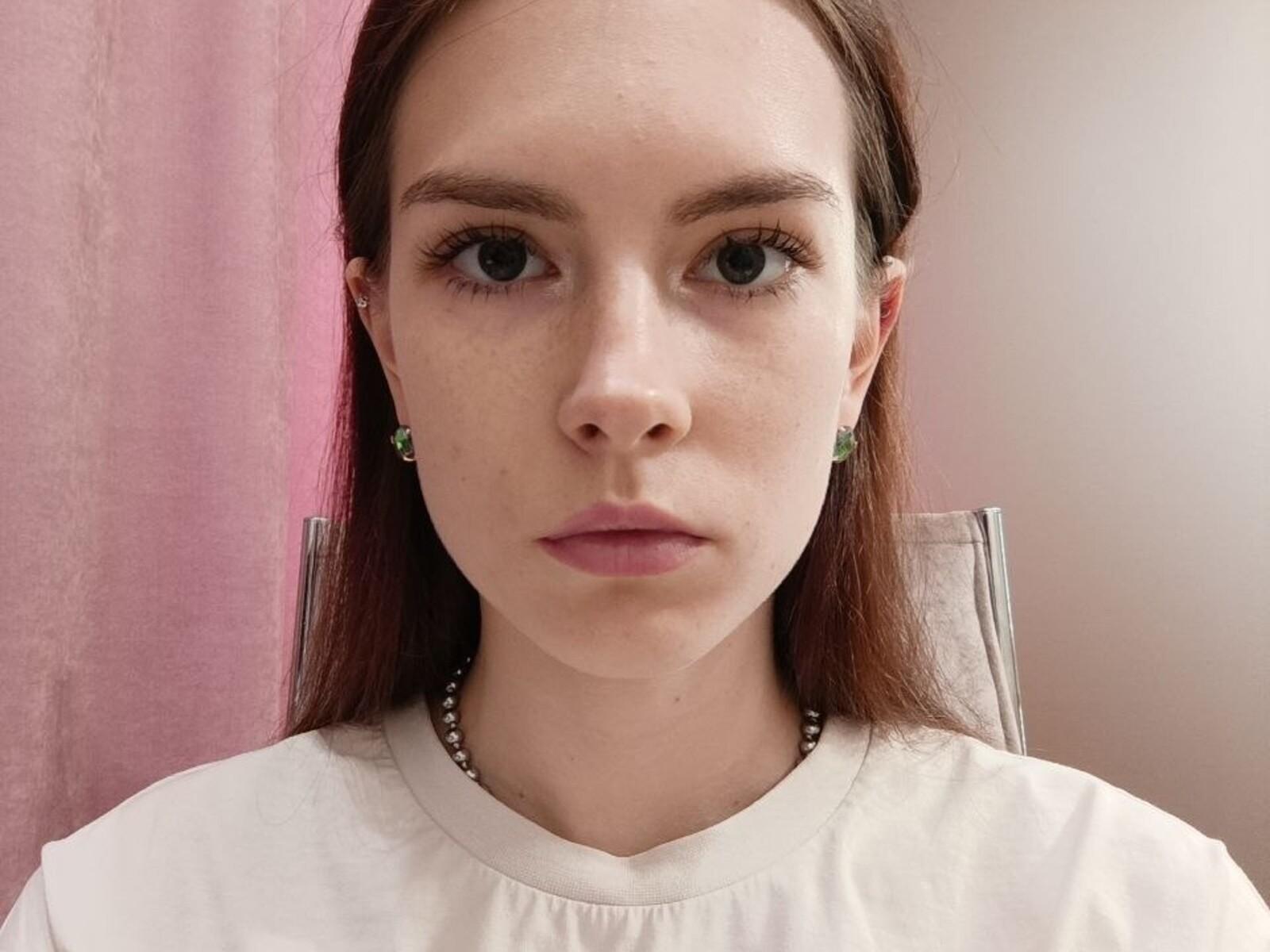 AmaliaCherubino heeft een ernstig gezicht, bleke huid, groene oorbellen, recht bruin haar en roze lippen. Ze draagt een witte blouse met een kralenketting..