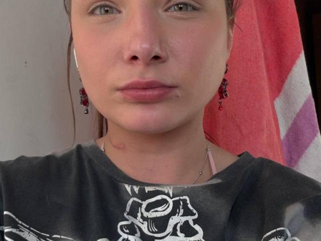 Patsy Bushmaker heeft een puistje op haar onderlip, draagt een zwart shirt met een roos dessin en heeft rode oorbellen. Haar huid is licht en haar ogen zijn groen..